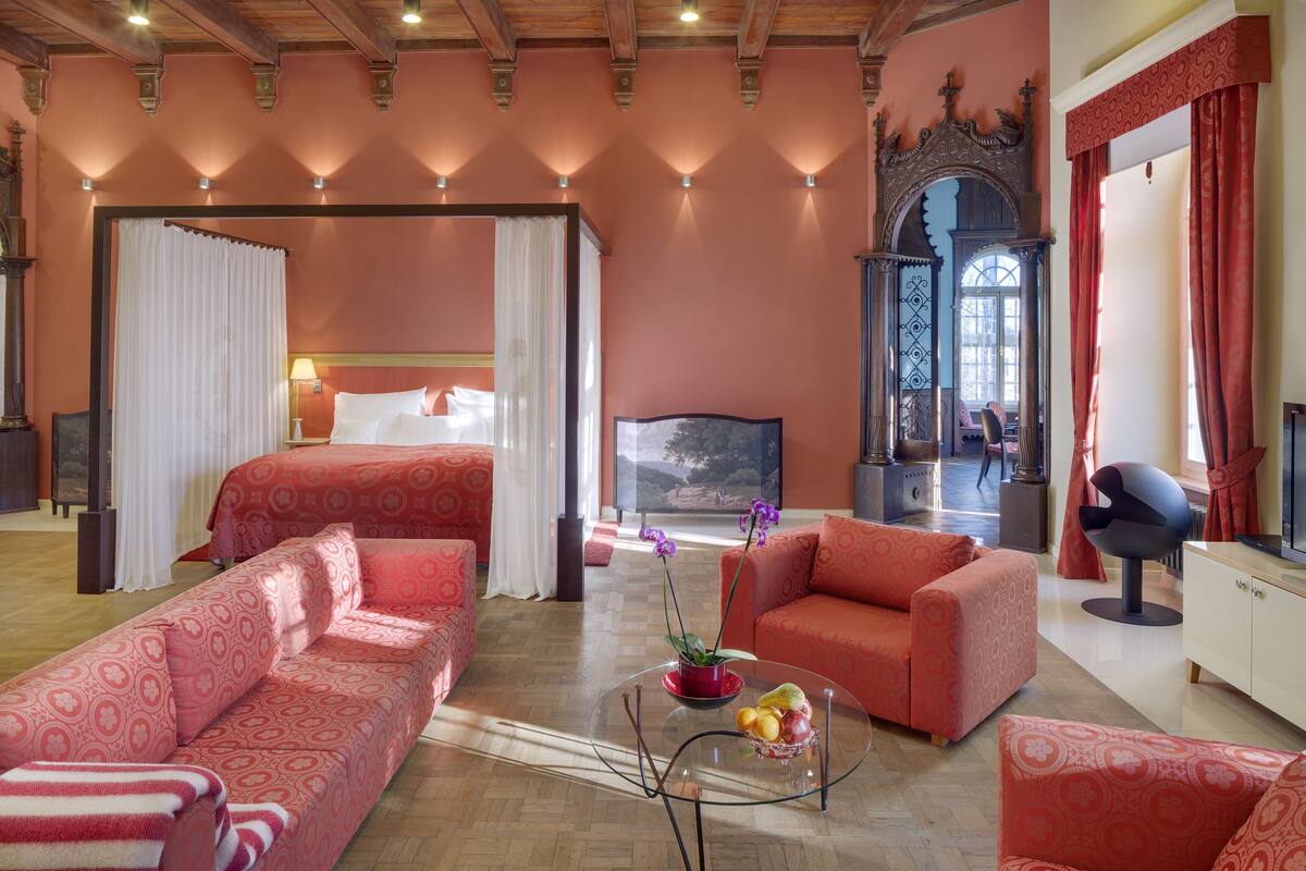 A hotel room with a large bed, two sofas, a glass coffee table with fruit, and a TV.