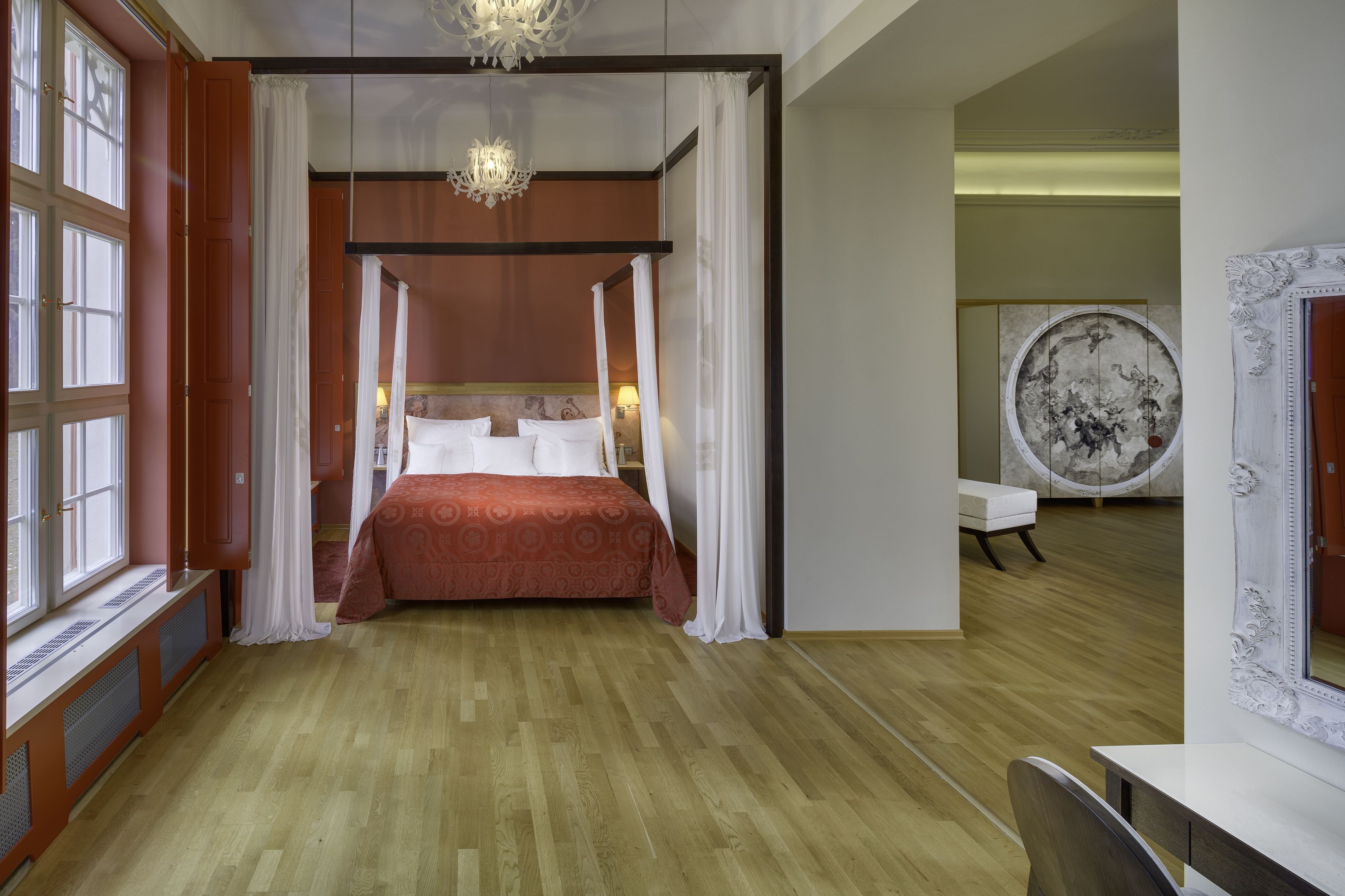 Quarto com uma cama grande, um candelabro, um espelho amplo e vista para a cidade.