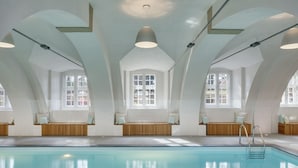 A swimming pool with a wooden deck and seating areas, large windows, and a high ceiling. - Chateau Herálec Boutique Hotel & Spa by L'OCCITANE (Heralec)