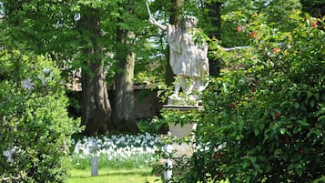A statue in a lush garden with trees and white flowers.