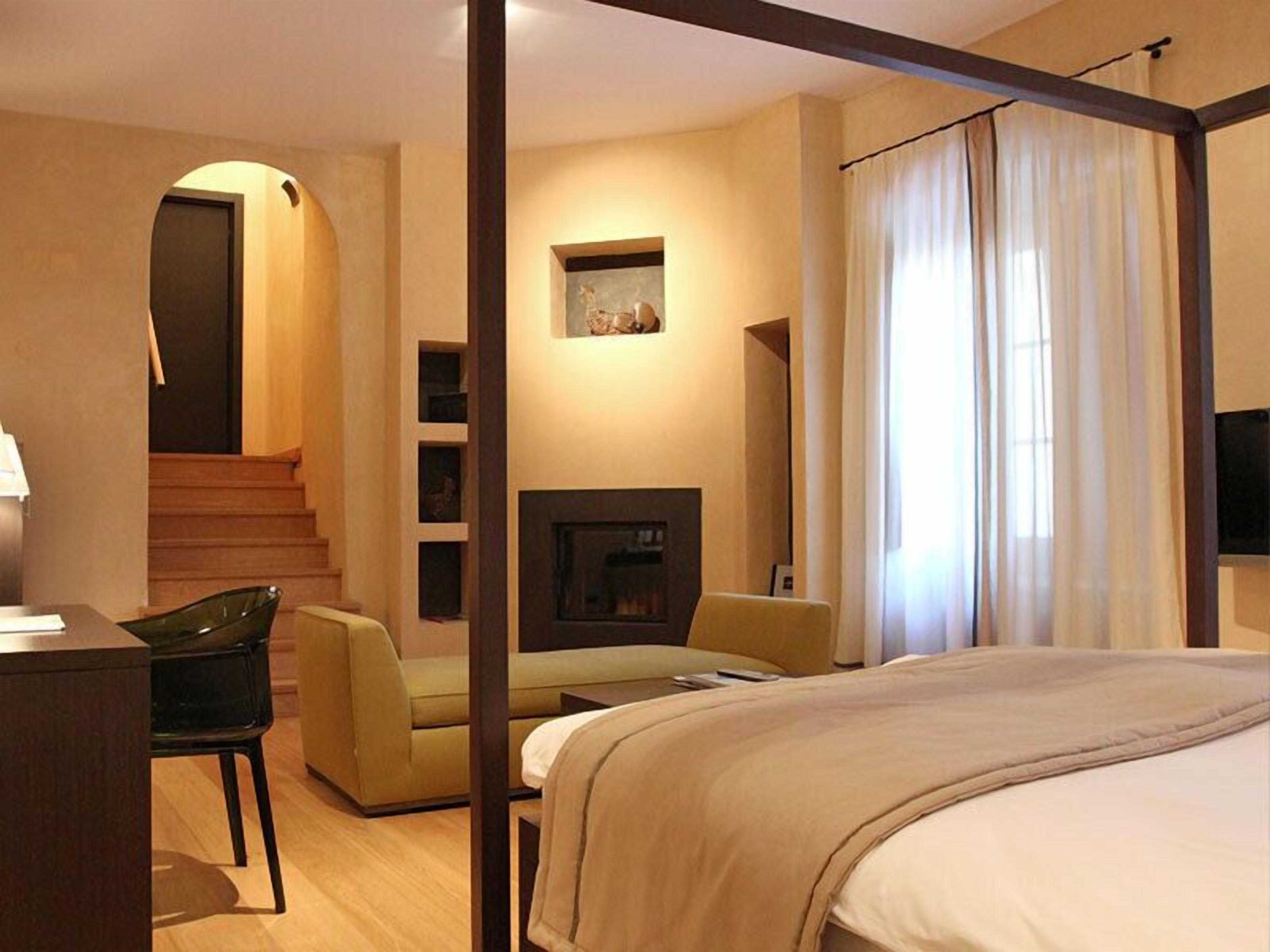 Quarto de hotel com cama, escrivaninha, cadeira, lareira e escada.