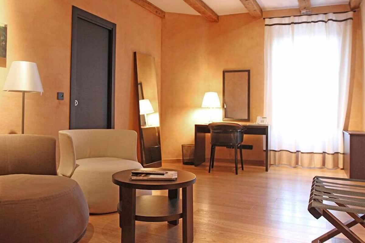 A hotel room with a sofa, a small round table, a desk with a chair, a lamp, and a large mirror.