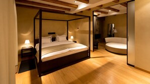 Una cama con dosel de madera, una mesita de noche con lámpara y un rincón de descanso circular.