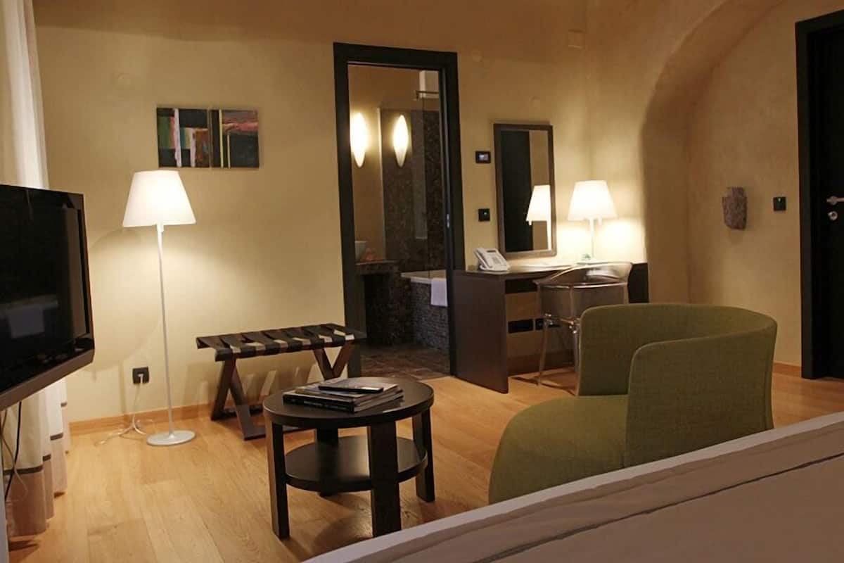 A hotel room with a TV, a desk with a chair, a small round table with books, and two lamps.