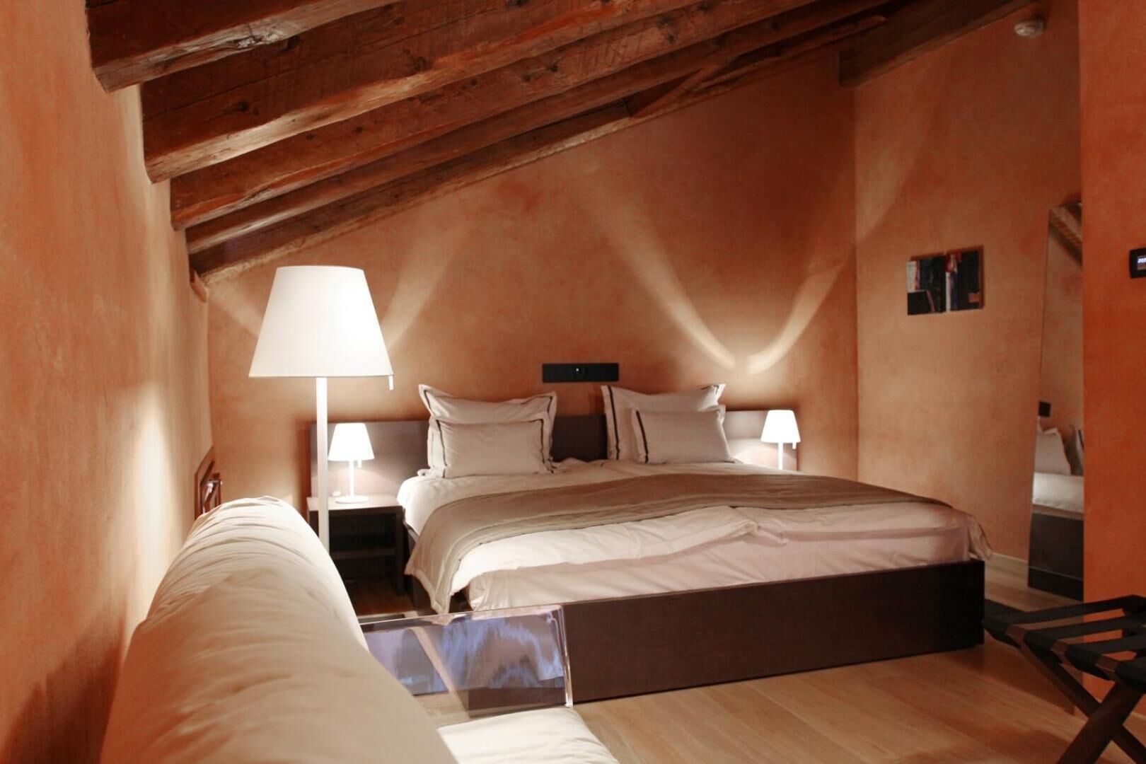 A bedroom with a wooden ceiling, a bed with white bedding, two bedside tables with lamps, and a small wooden chair.