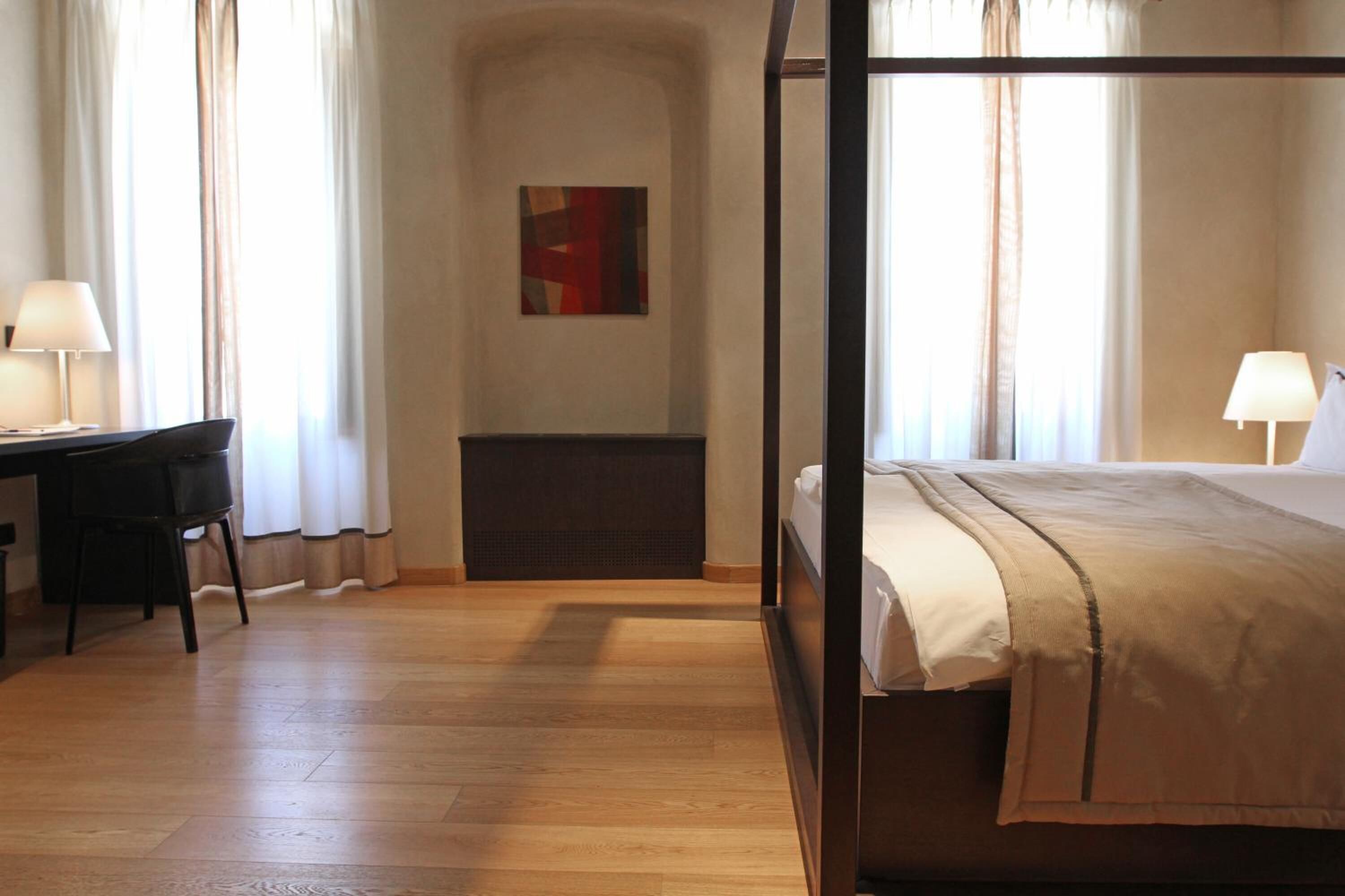 A hotel room with a four-poster bed, a desk with a chair, and a radiator.