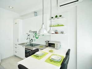 Una cucina moderna con mobili bianchi, un forno a microonde, un lavello e un'area pranzo con un tavolo imbandito per due persone.