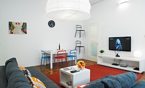 Un salon moderne avec un canapé, une table à manger et des chaises, un téléviseur et une horloge au mur.