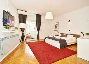 Une chambre d’hôtel moderne avec un grand lit, un tapis rouge, une télévision, un bureau et une fenêtre avec des rideaux.