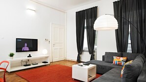 A modern living room with a grey sofa, a white coffee table, a red rug, a TV on the wall, and black curtains.