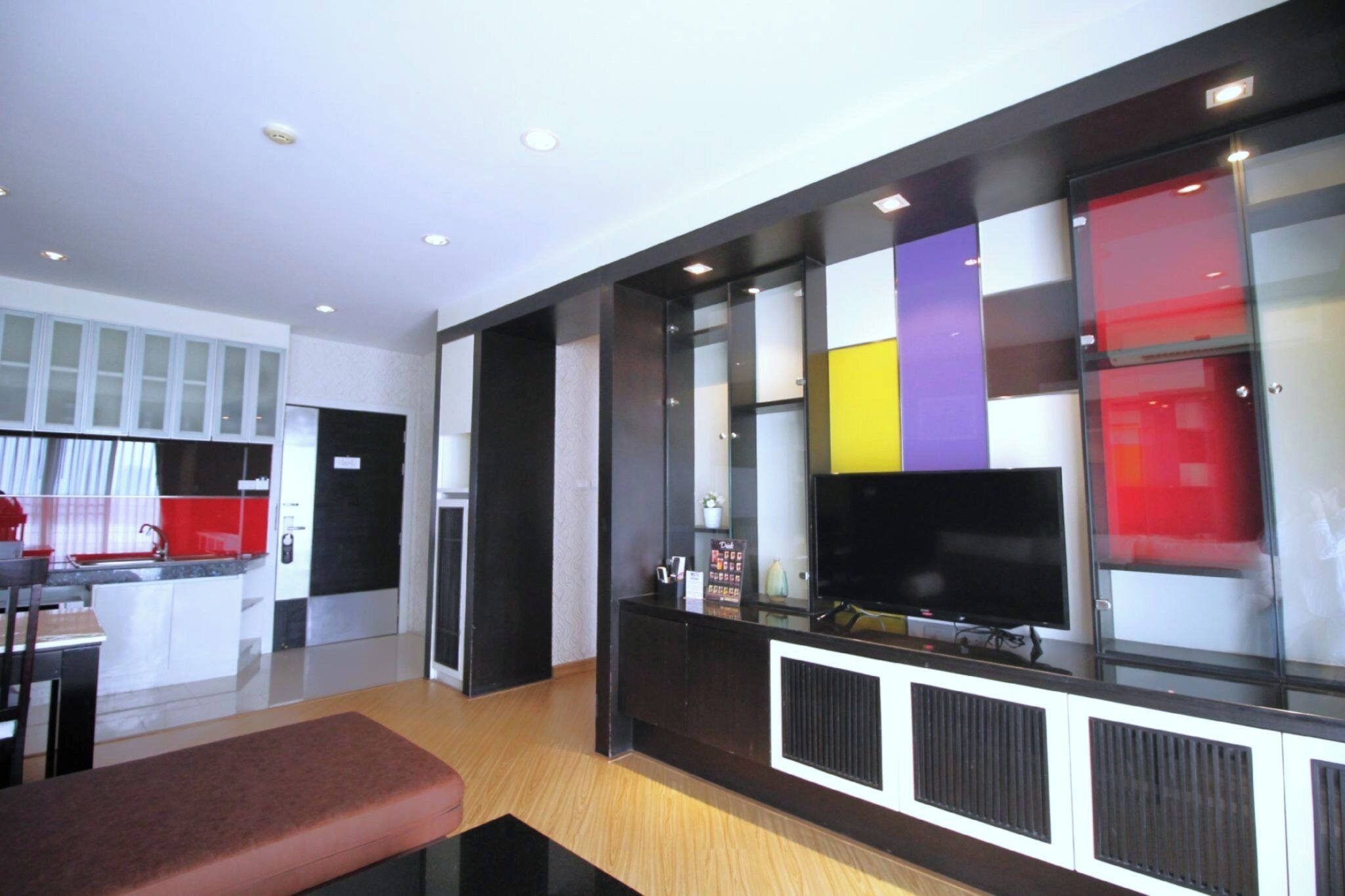 Cuina moderna amb frigorífic integrat, zona de menjador amb banquetes i un televisor fixat a un módul negre amb panells de colors.