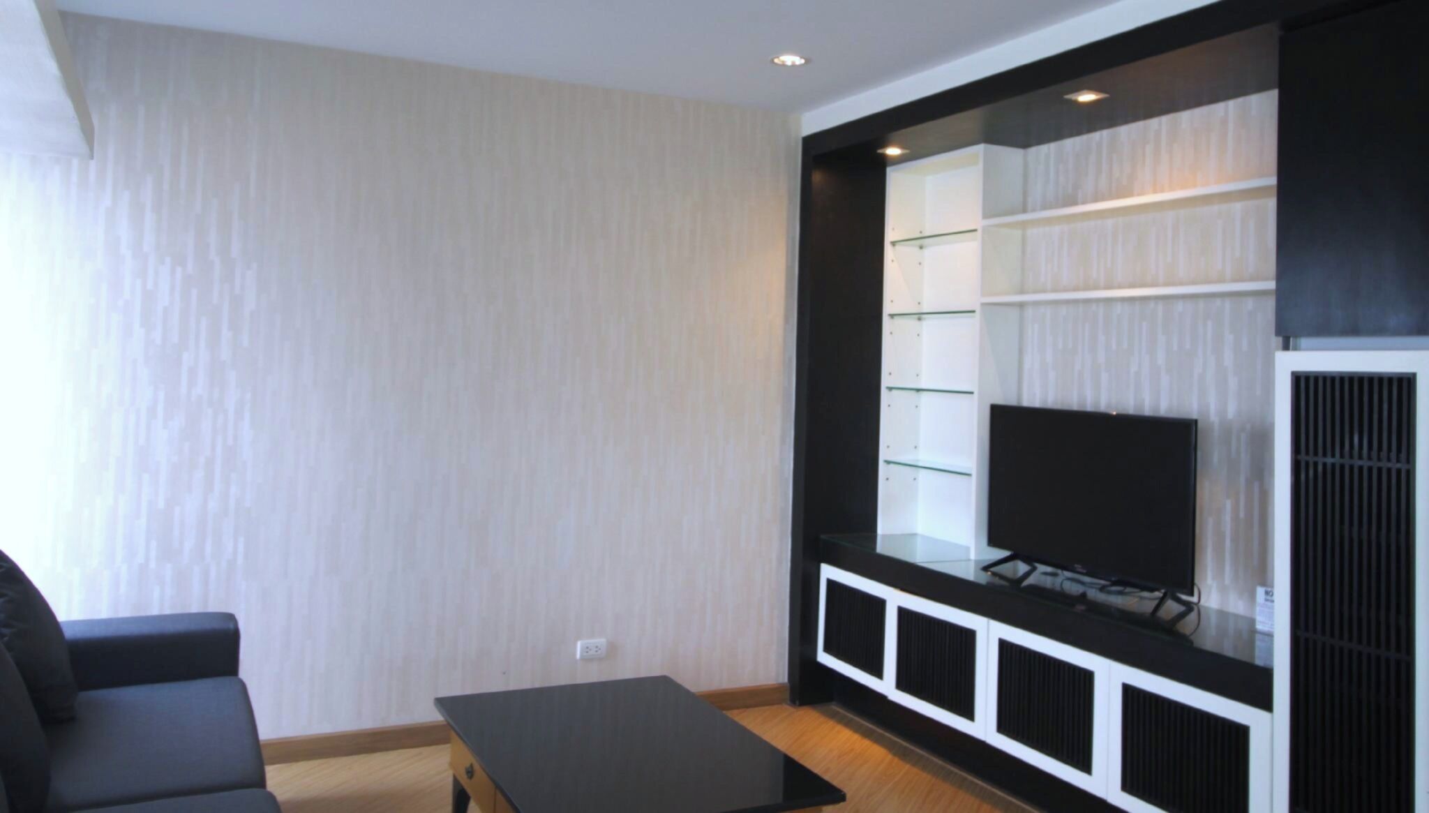 A modern living room with a flat-screen TV, a black sofa, and a glass-fronted entertainment unit.