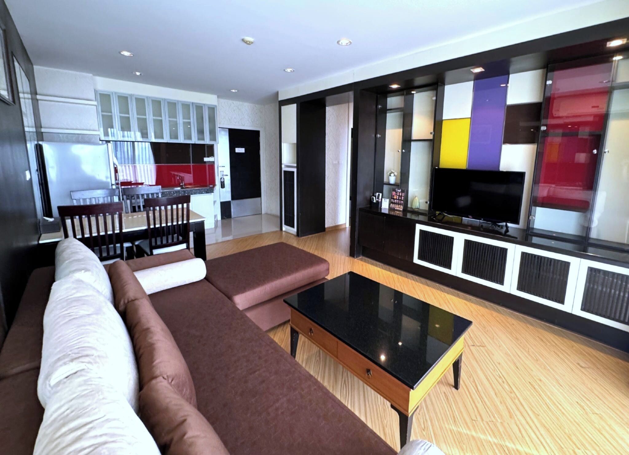Una sala de estar moderna con un sofá, una mesa de centro y un televisor. Se observa una cocina al fondo con armarios y una mesa de comedor.