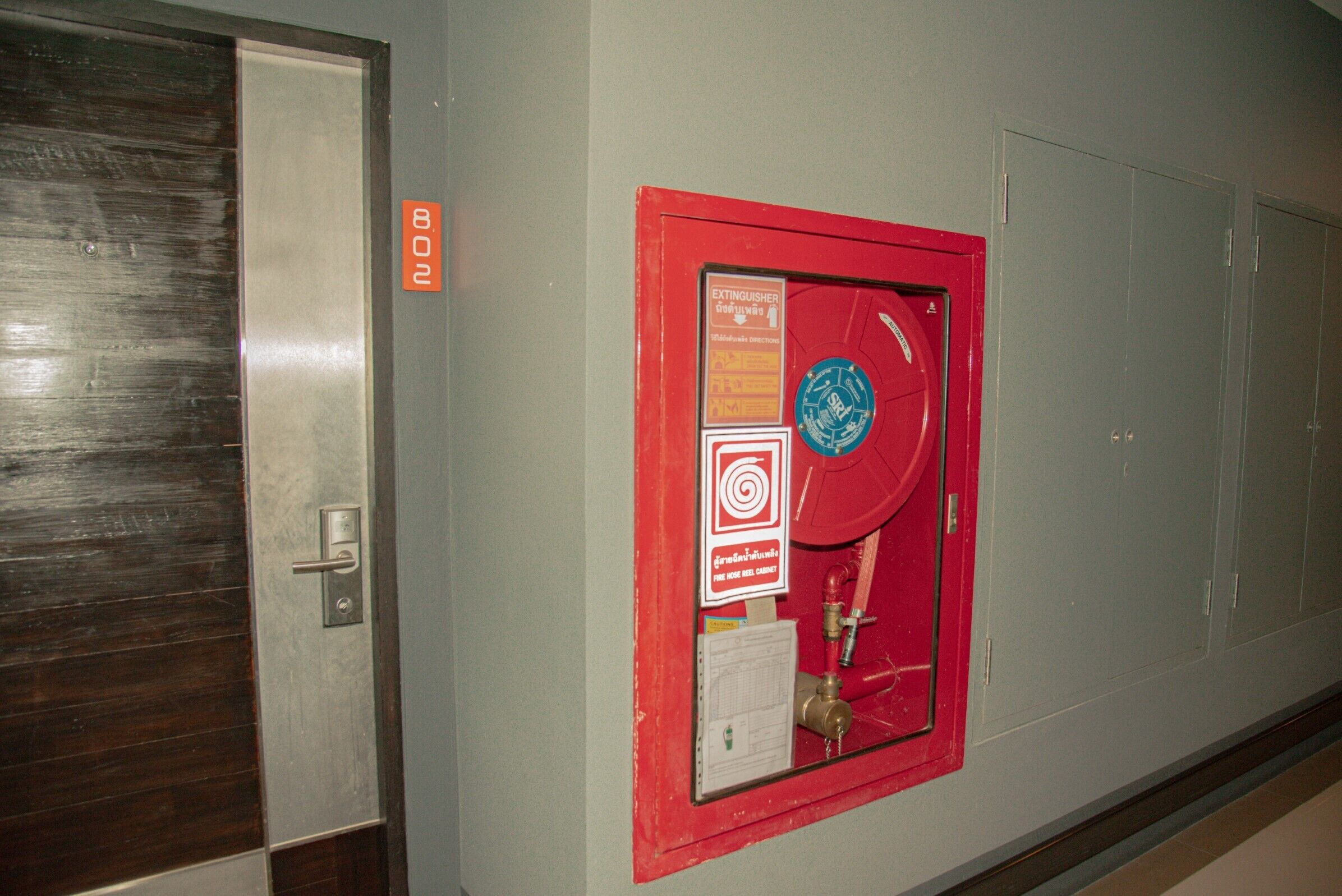 A hallway with a fire extinguisher mounted on the wall, a door with a number sign, and a fire safety sign.