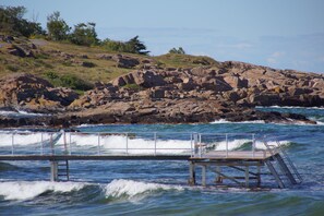 A rocky shoreline with a pier extending into the water. - Hotel Sandvig Havn (Allinge)