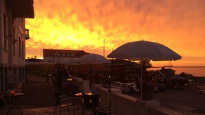 A terrace with outdoor seating, overlooking a beach and a sunset. - Hotel Sandvig Havn (Allinge)