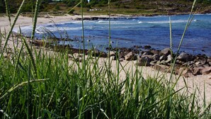 A beach with green grass in the foreground, a rocky shoreline, and waves crashing onto the sand. - Hotel Sandvig Havn (Allinge)