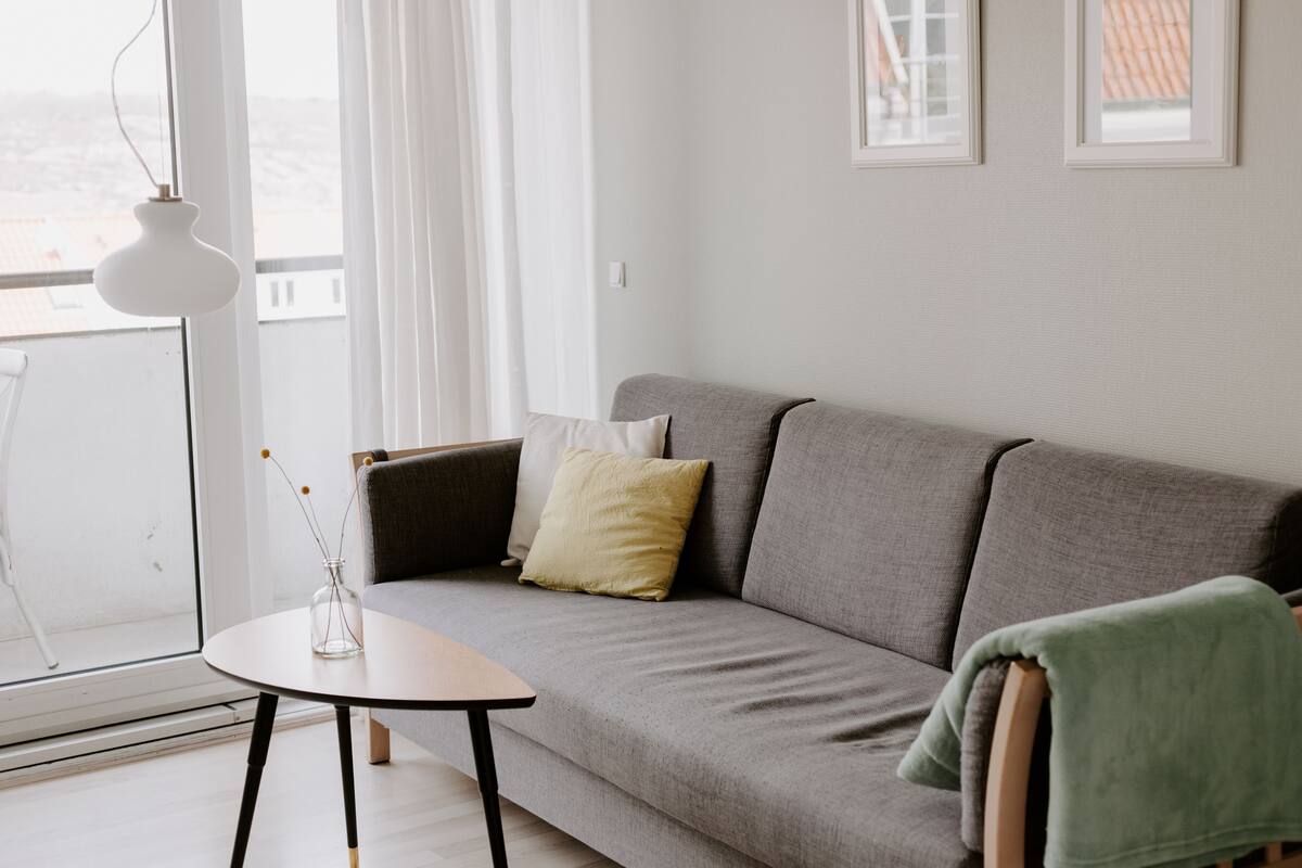 A modern living room with a grey sofa, a small round table, and a view through a large window.