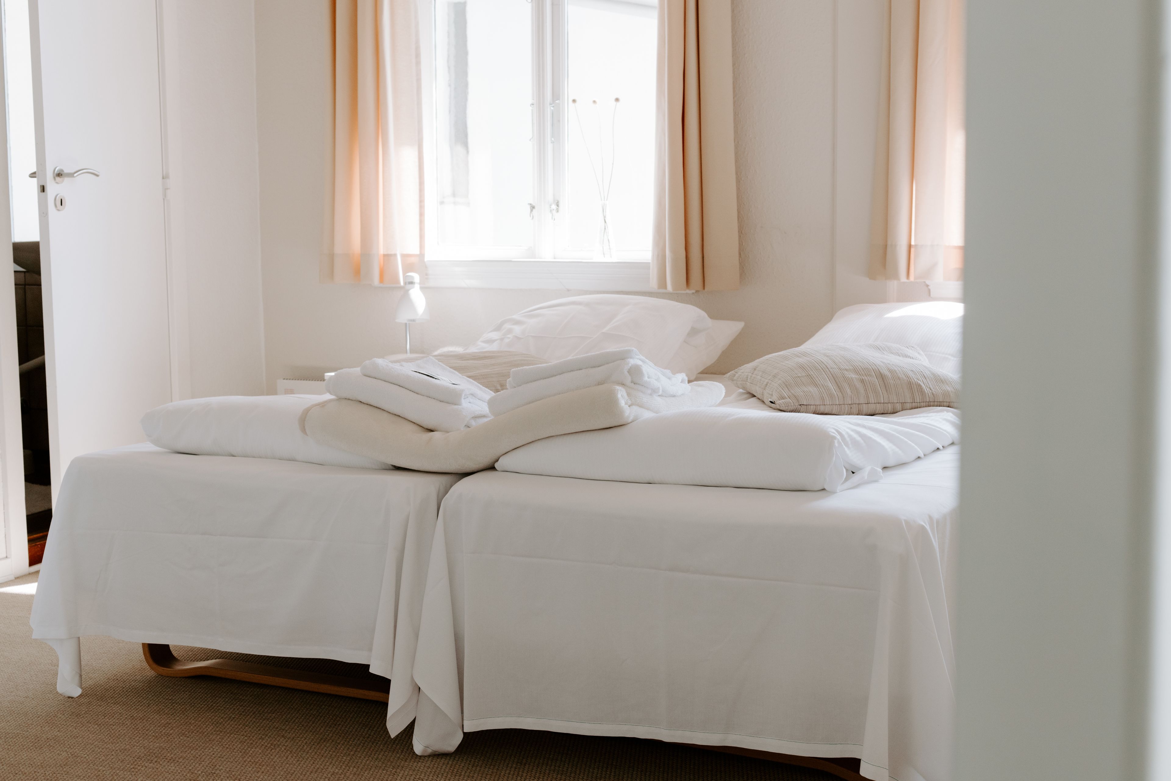 A double bed with white bedding, a bedside table, and a window with curtains.