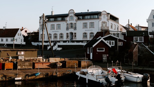 A waterfront property with a large white building, a dock with boats, and a small red building. - Hotel Sandvig Havn (Allinge)