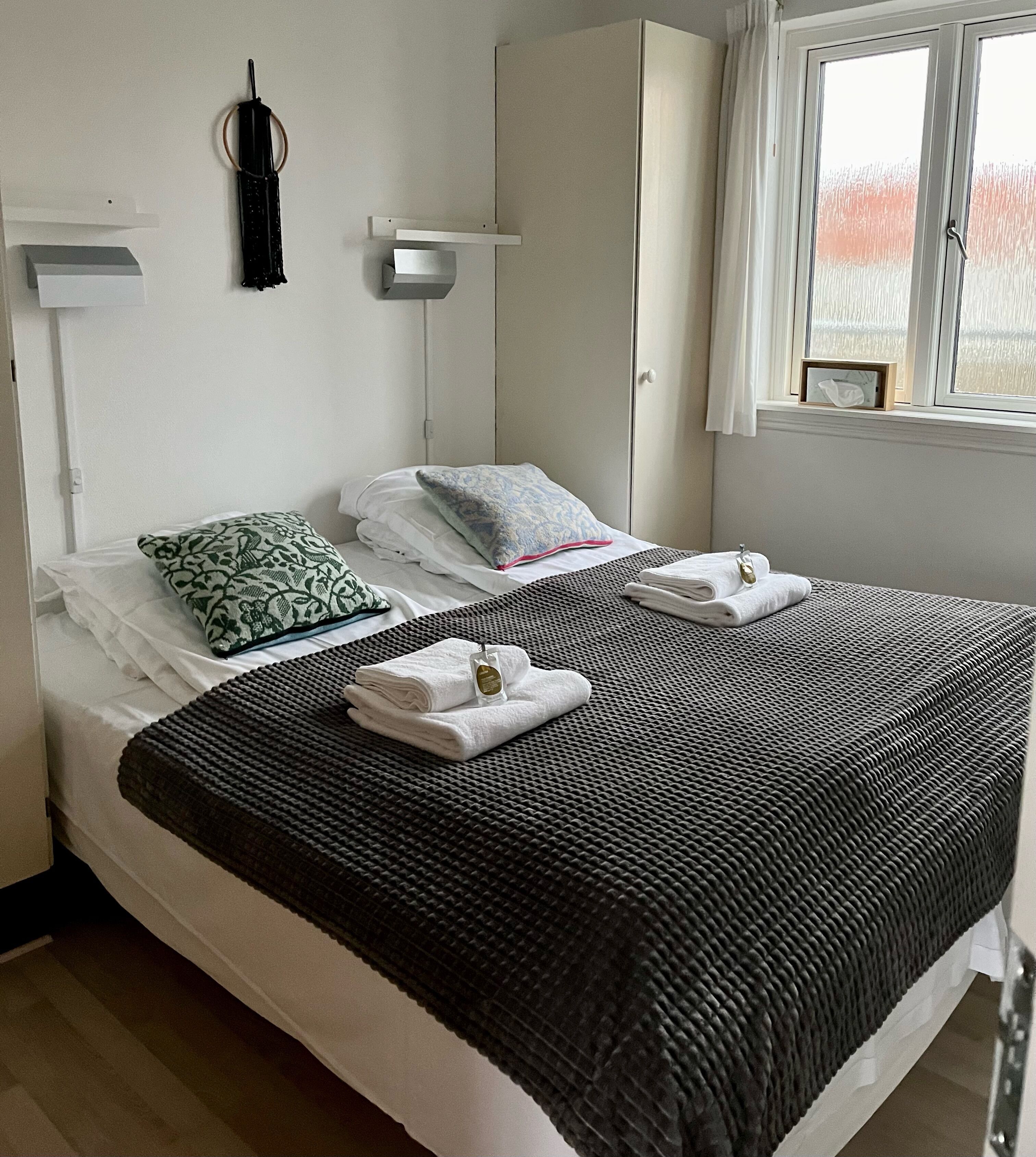 A neatly made bed with a black and white patterned bedspread, white pillows, and folded towels.