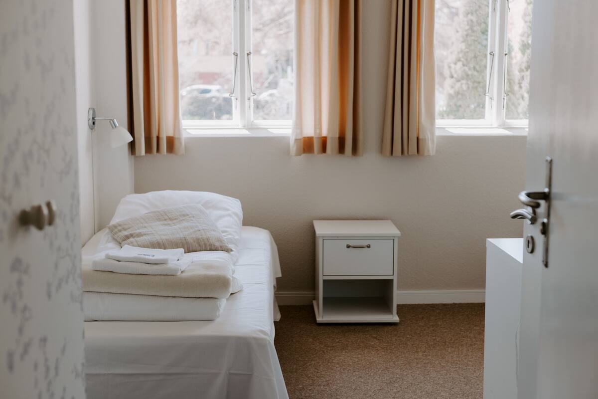 A bedroom with a bed, bedside table, and a window with curtains.