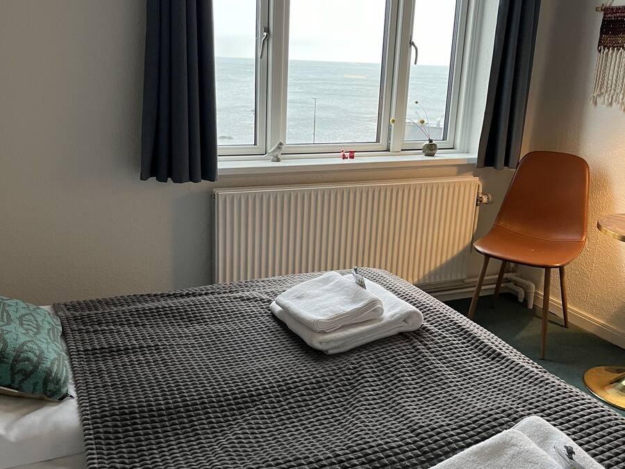 Habitación de hotel con cama, vista al mar a través de una ventana, una silla y un radiador.