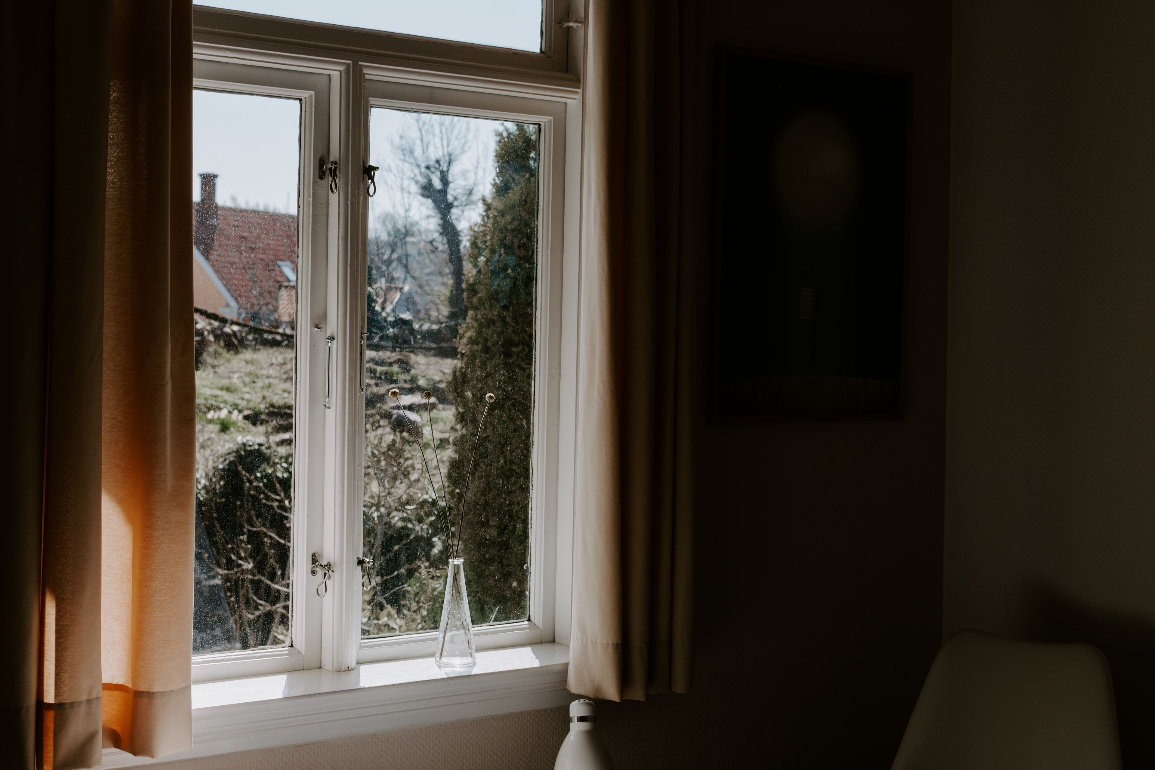 Ein Zimmer mit Fenster, einer Vase und einem Bild an der Wand.