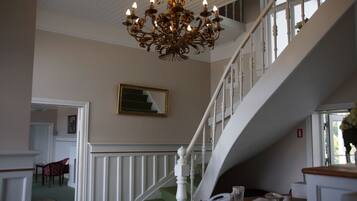 Eine prächtige Treppe mit weißen Balustraden und einem grünen Teppich führt zu einer oberen Etage. Ein Kronleuchter hängt von der Decke, und ein gerahmtes Bild ist an der Wand sichtbar.