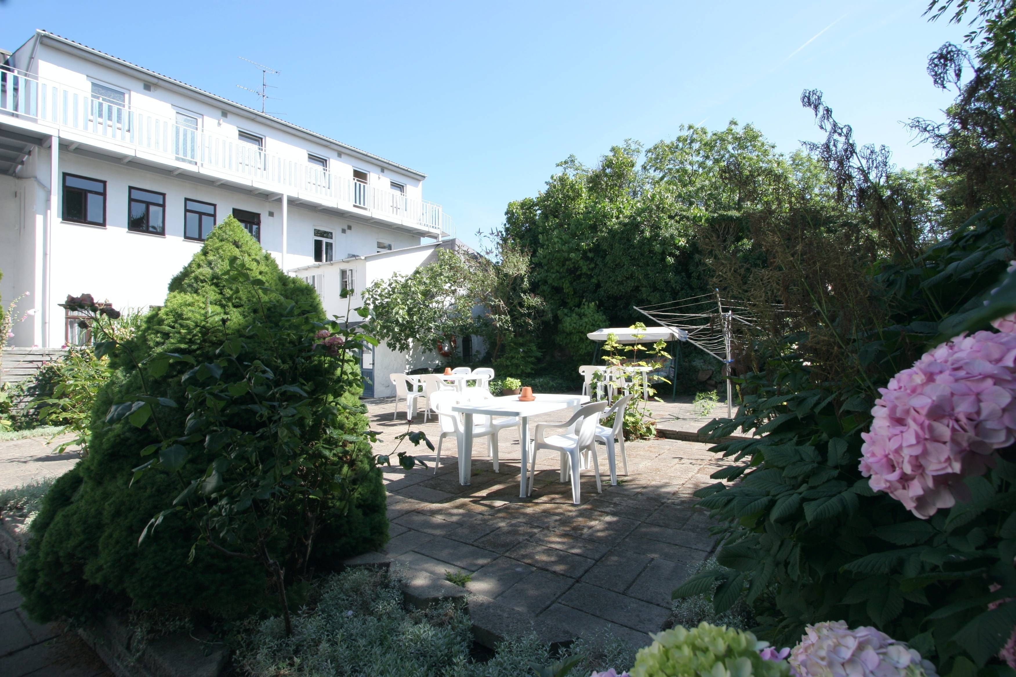 A courtyard with a white building, outdoor seating, and lush greenery.