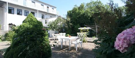 A courtyard with a white building, outdoor seating, and lush greenery.
