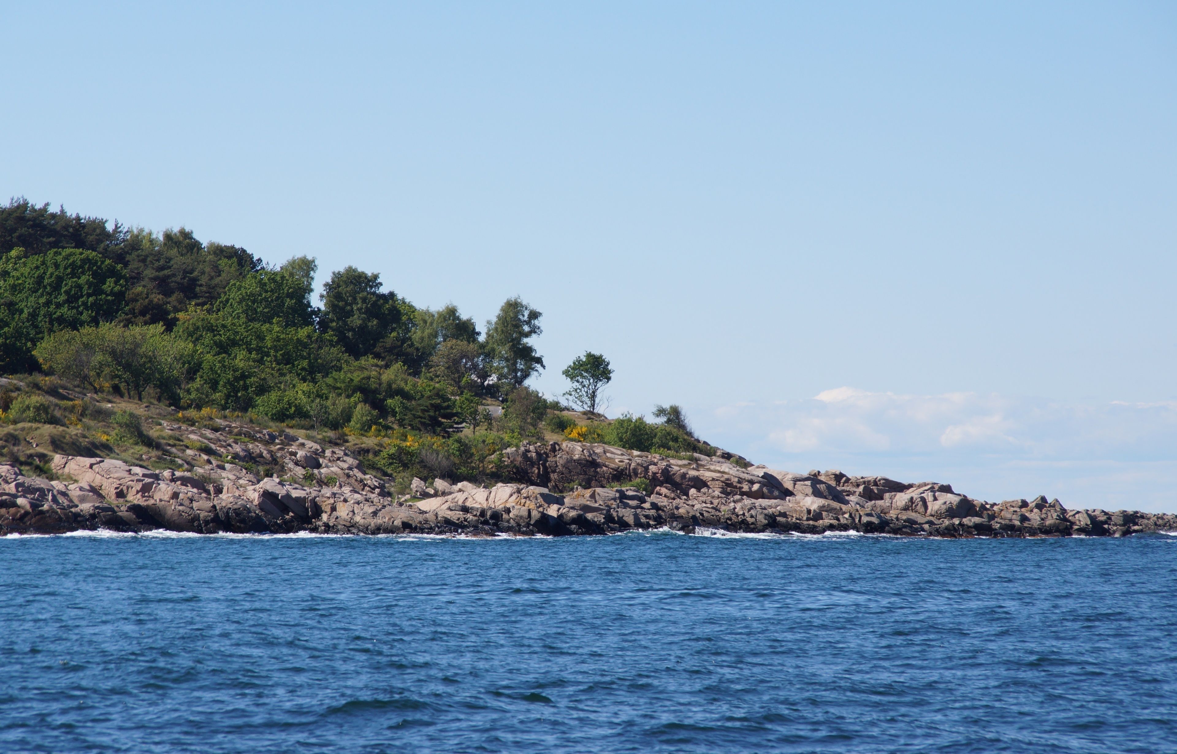 Une côte rocheuse bordée d’une mer d’un bleu profond et d’une colline boisée.