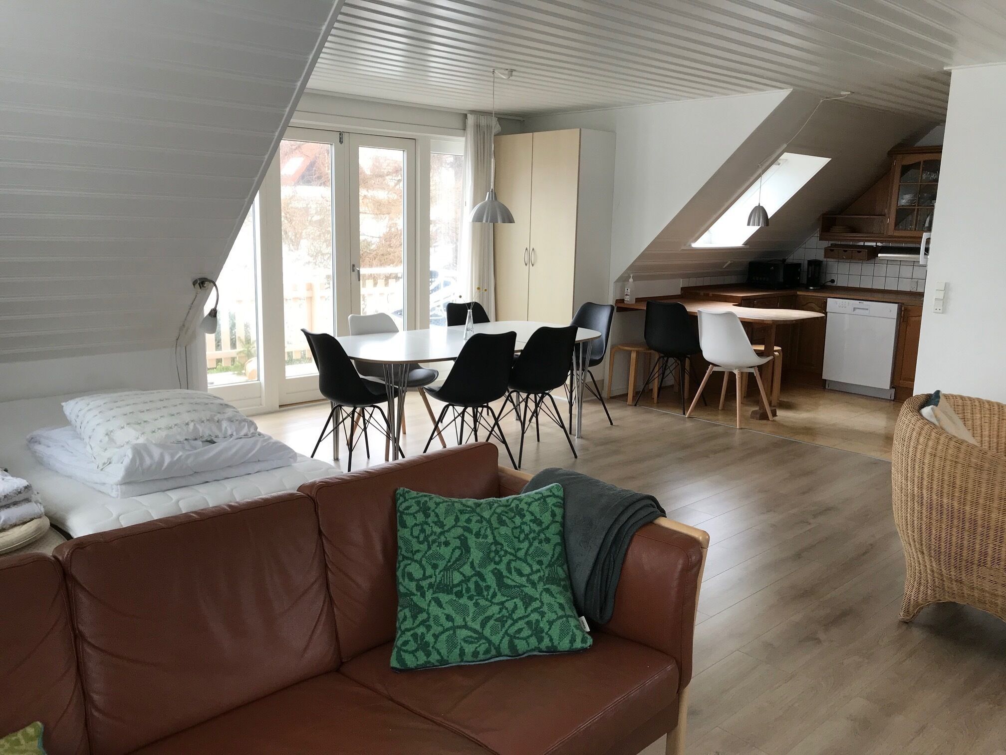 A modern loft-style living space with a dining area, kitchenette, and large windows.