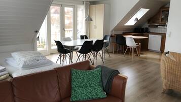 A modern loft-style living space with a dining area, kitchenette, and large windows.
