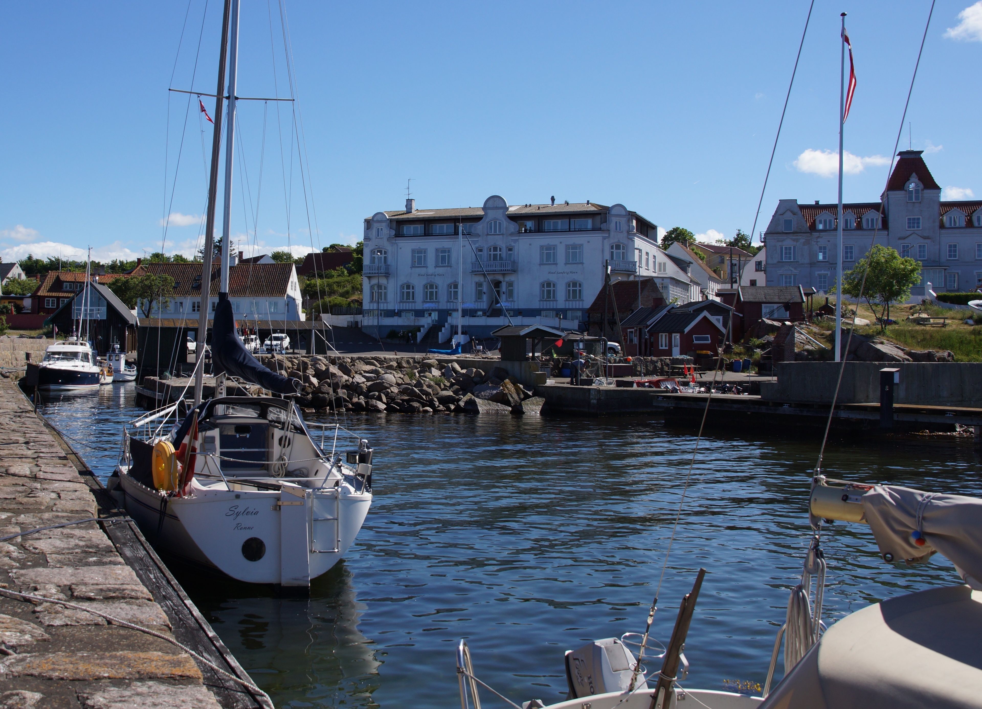 A harbor with boats docked, a stone quay, and buildings in the background.