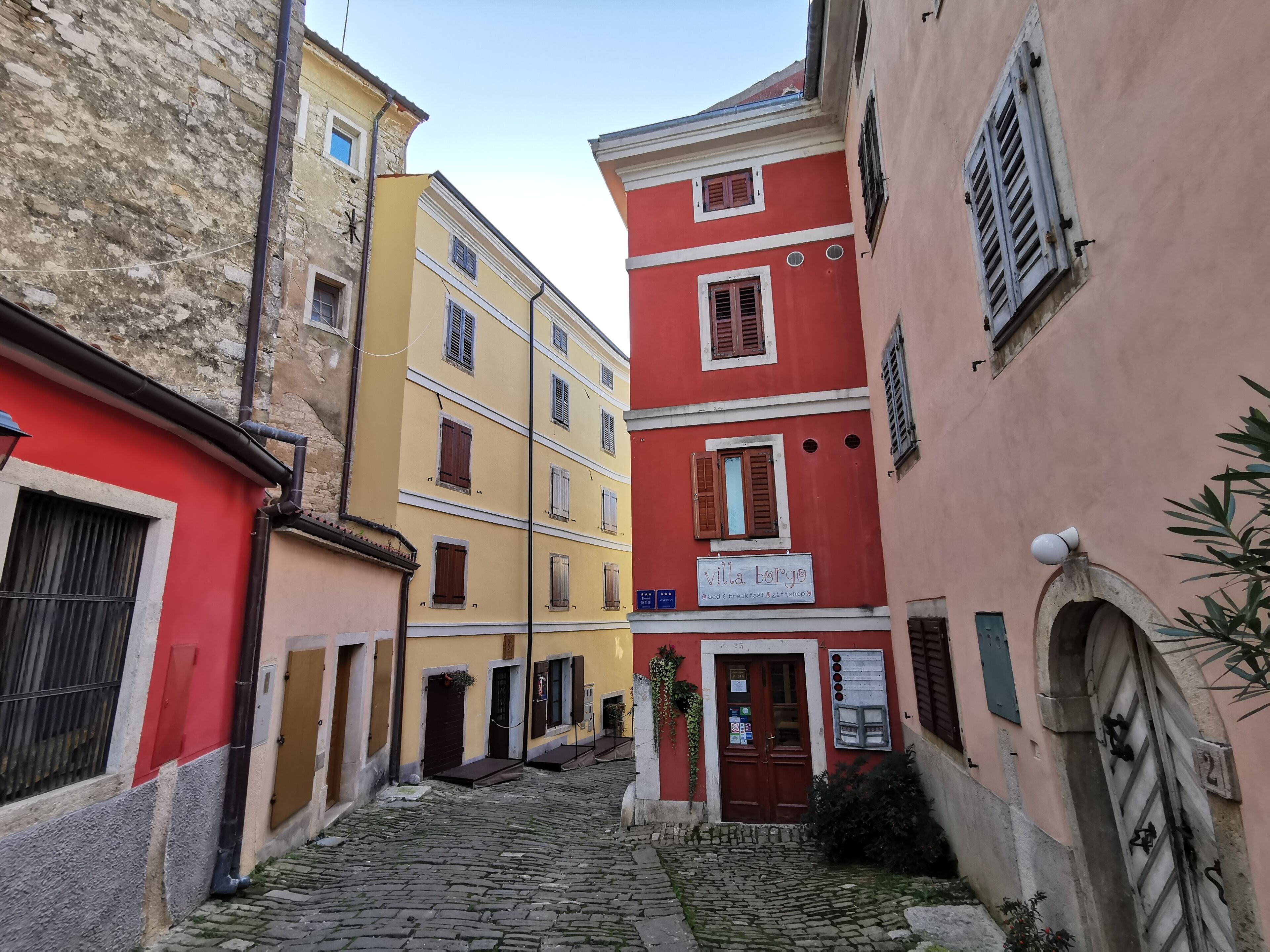 Una estrecha calle adoquinada con edificios de arquitectura tradicional, incluyendo un cartel que indica 'villa borgo', una casa de huéspedes.