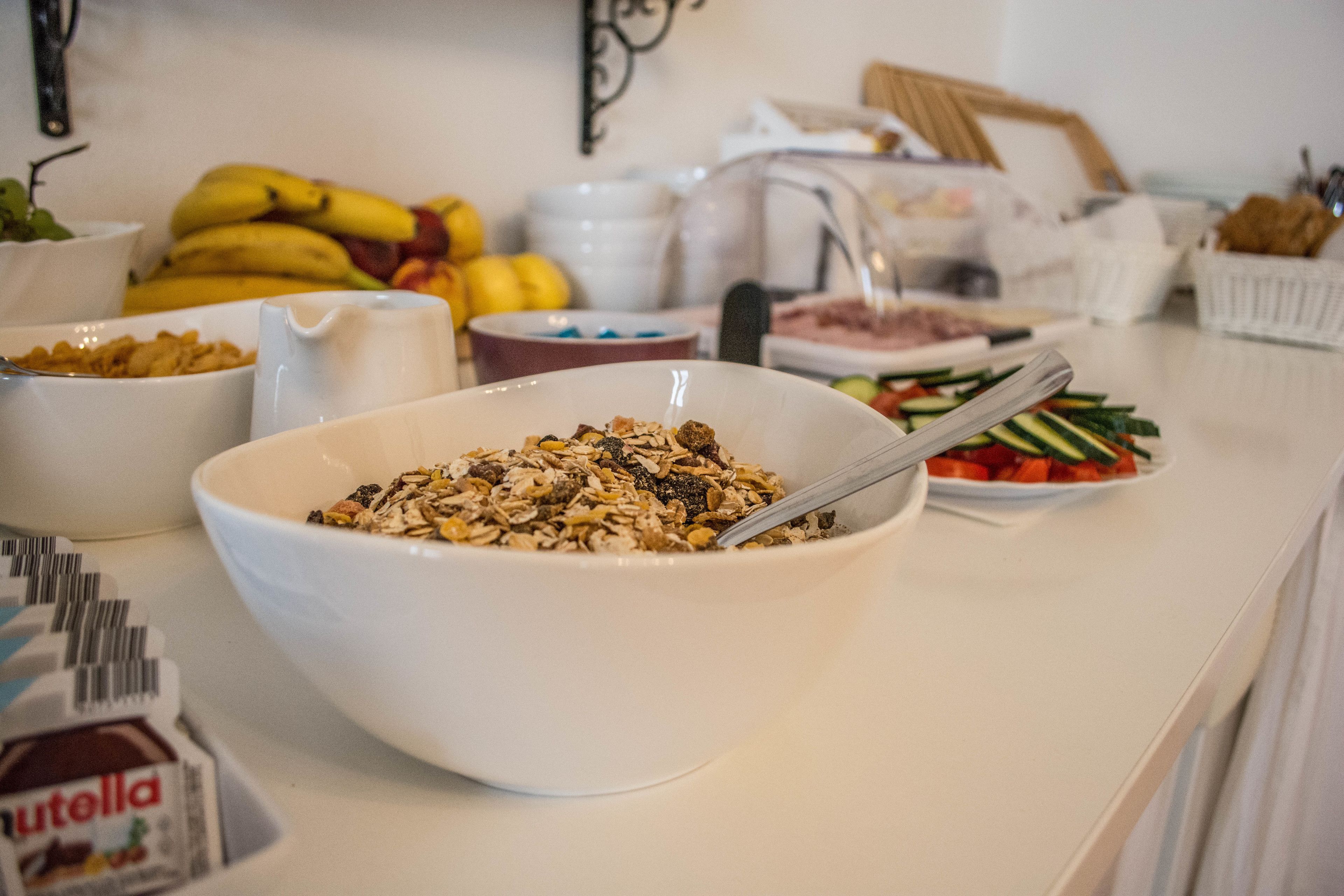 En buffet med forskellige retter, herunder en skål granola, en skål frugt og et fad med skivede grøntsager.