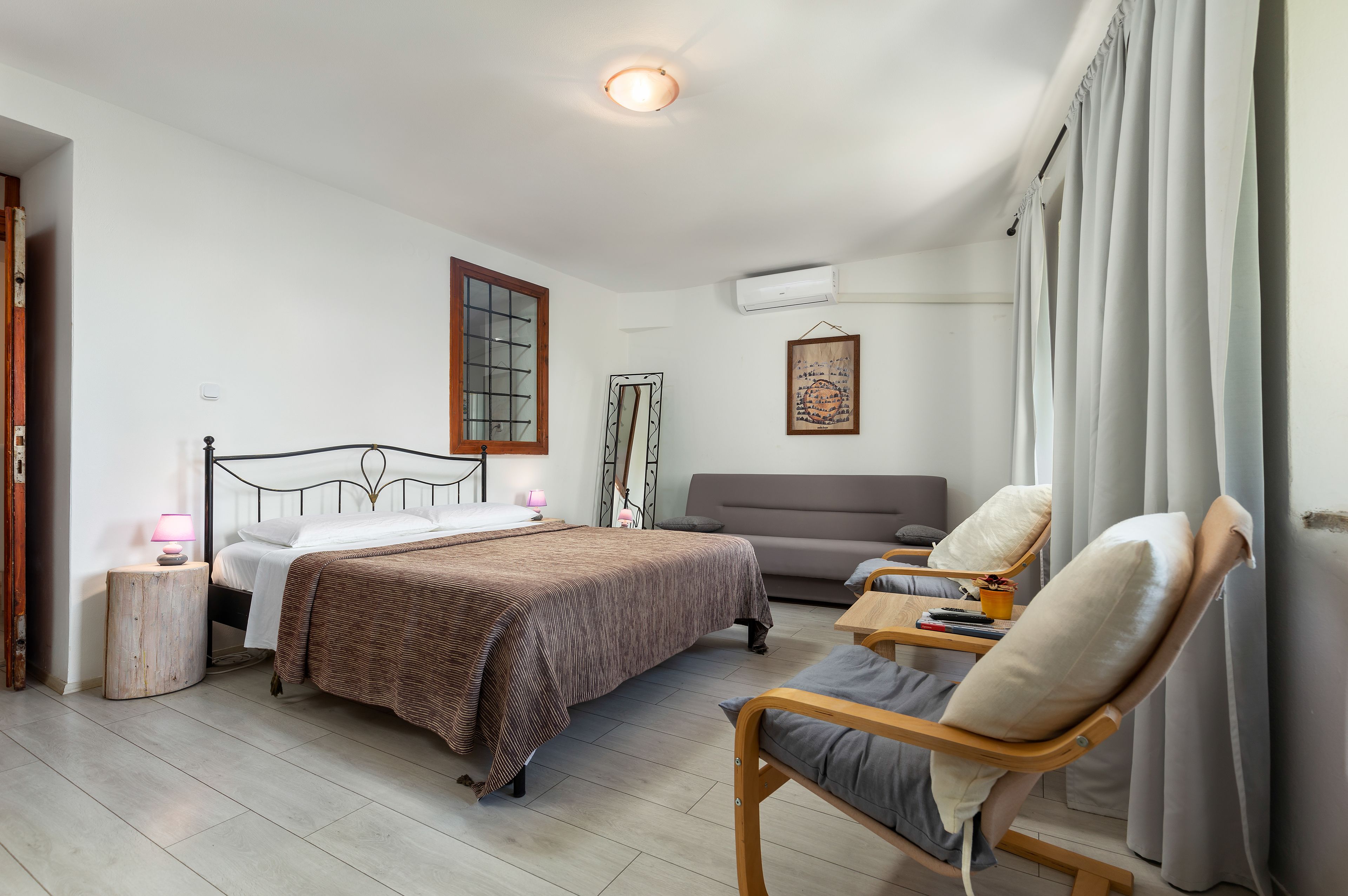 A hotel room with a bed, a sofa, a chair, a small table, and a window with curtains.