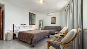 A hotel room with a bed, a sofa, a chair, a small table, and a window with curtains.