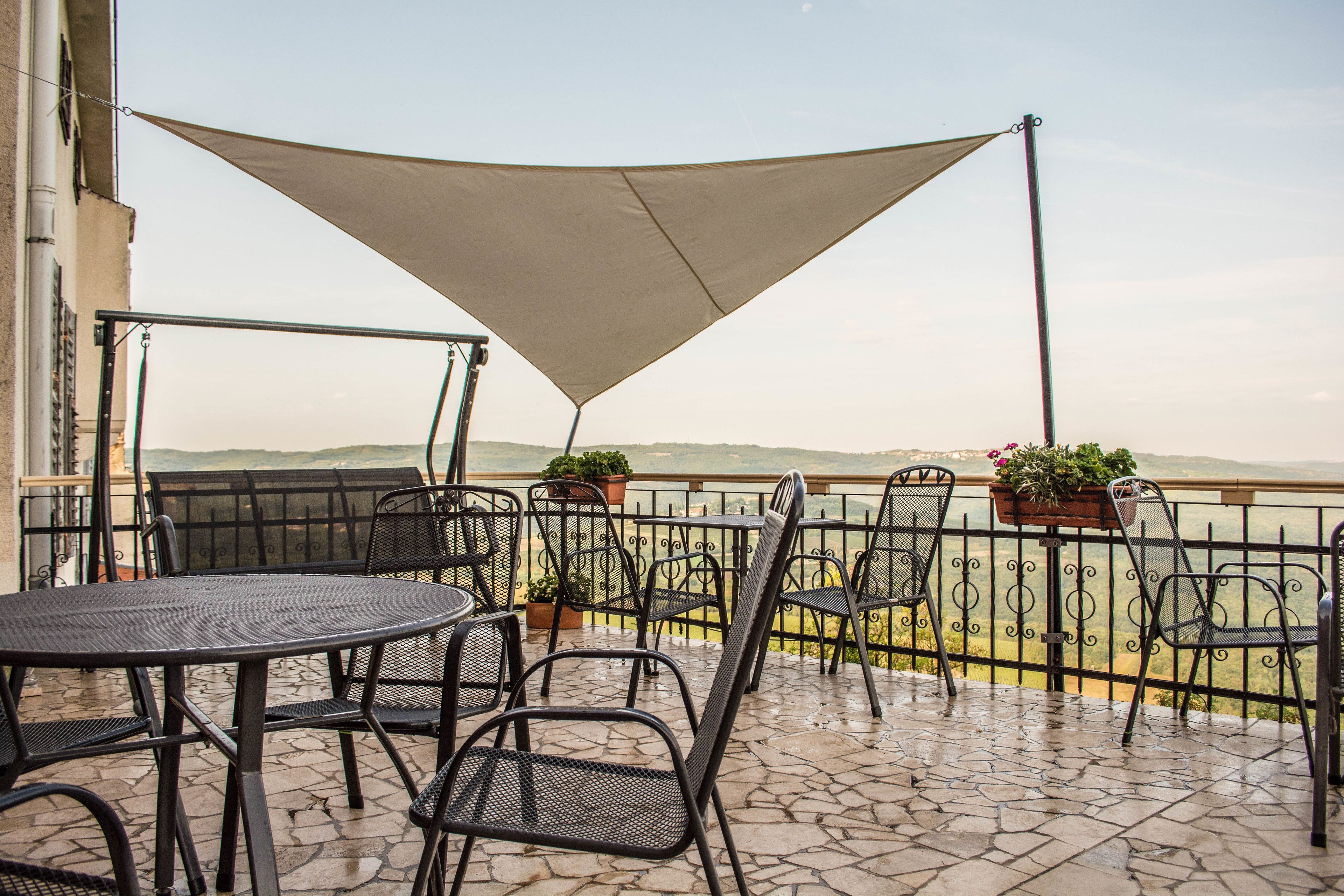 An outdoor patio with a table and chairs, a large shade sail, and potted plants.