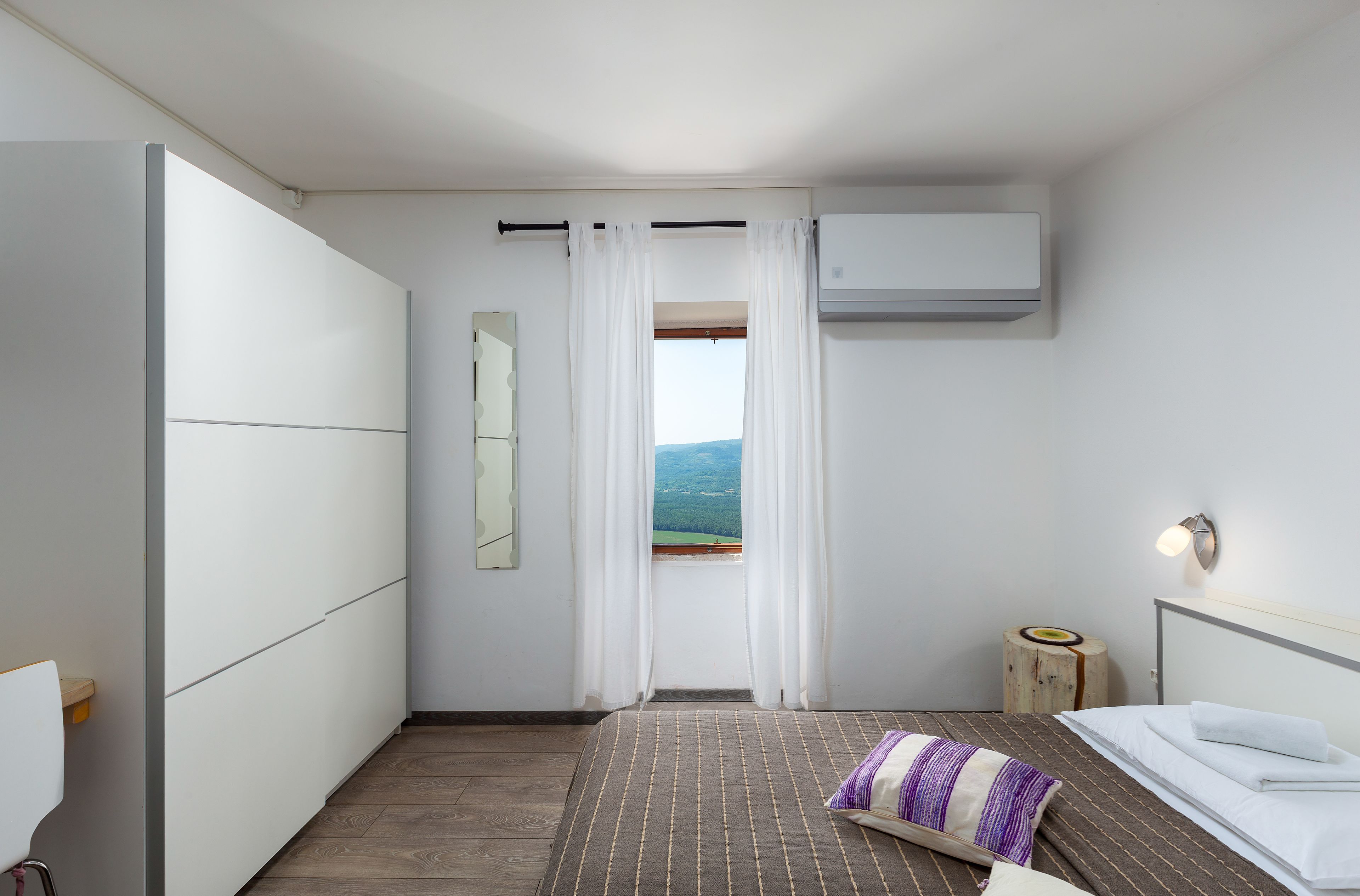 Une chambre d’hôtel moderne équipée d’un lit, d’une table de chevet, d’un miroir et d’une fenêtre avec des rideaux.