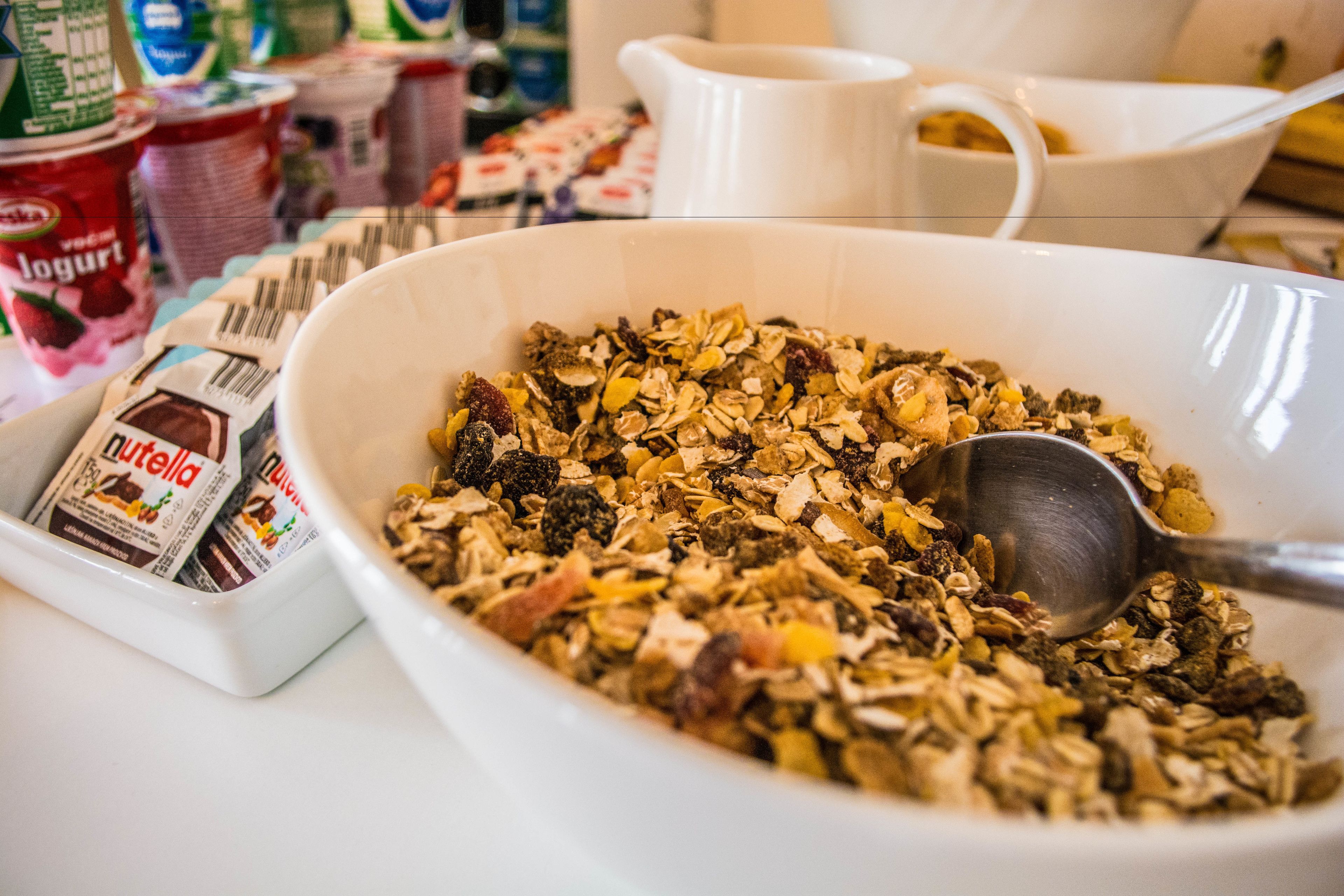 Un tazón de granola con una cuchara, rodeado de diferentes alimentos y recipientes.
