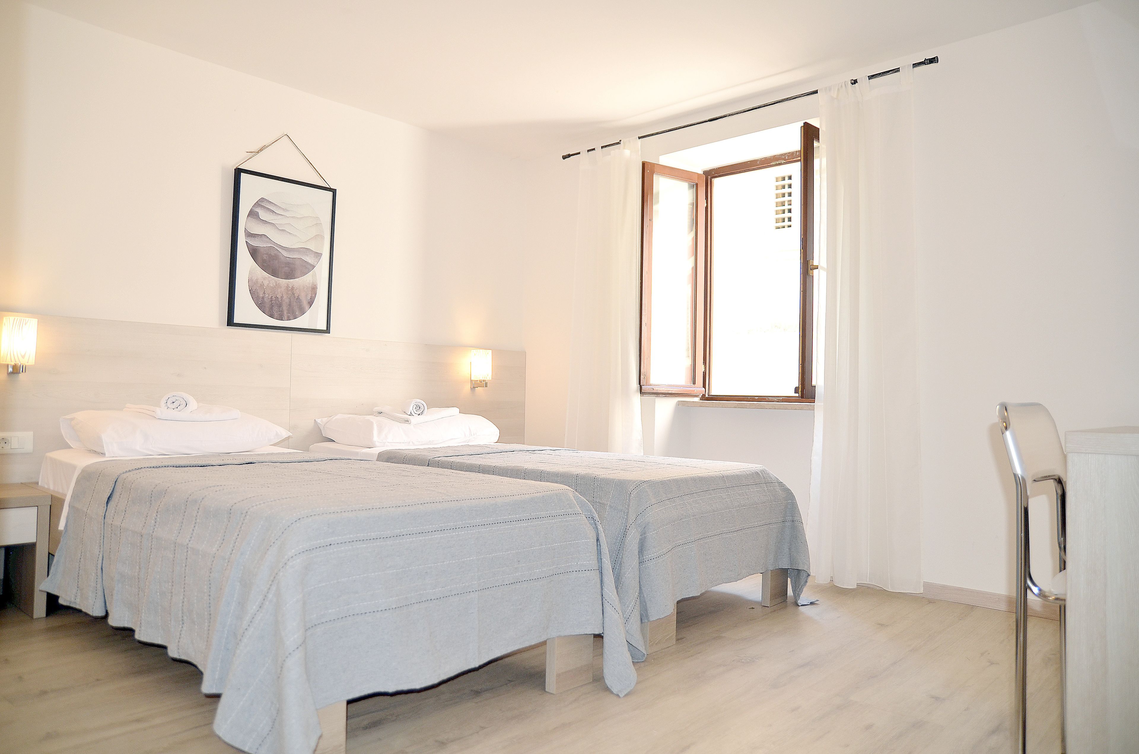 A hotel room with two beds, a large window, and a wall-mounted artwork.