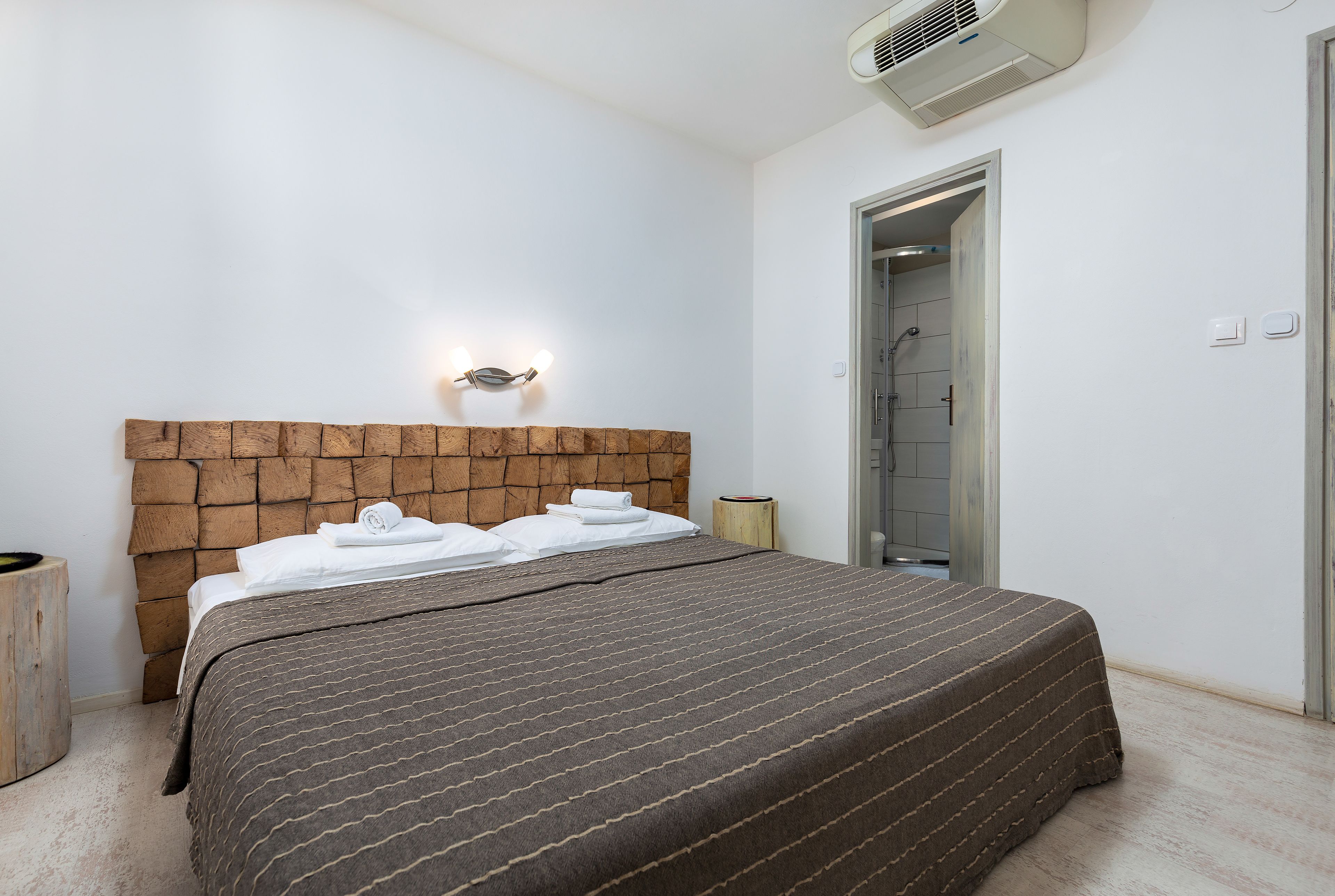 Un dormitorio con cabecera de madera, una cama con colcha a rayas marrones, una mesita de noche con lámpara y una puerta que da al baño.