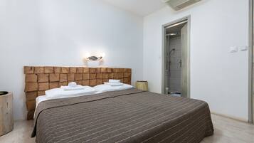 Un dormitorio con cabecera de madera, una cama con colcha a rayas marrones, una mesita de noche con lámpara y una puerta que da al baño.