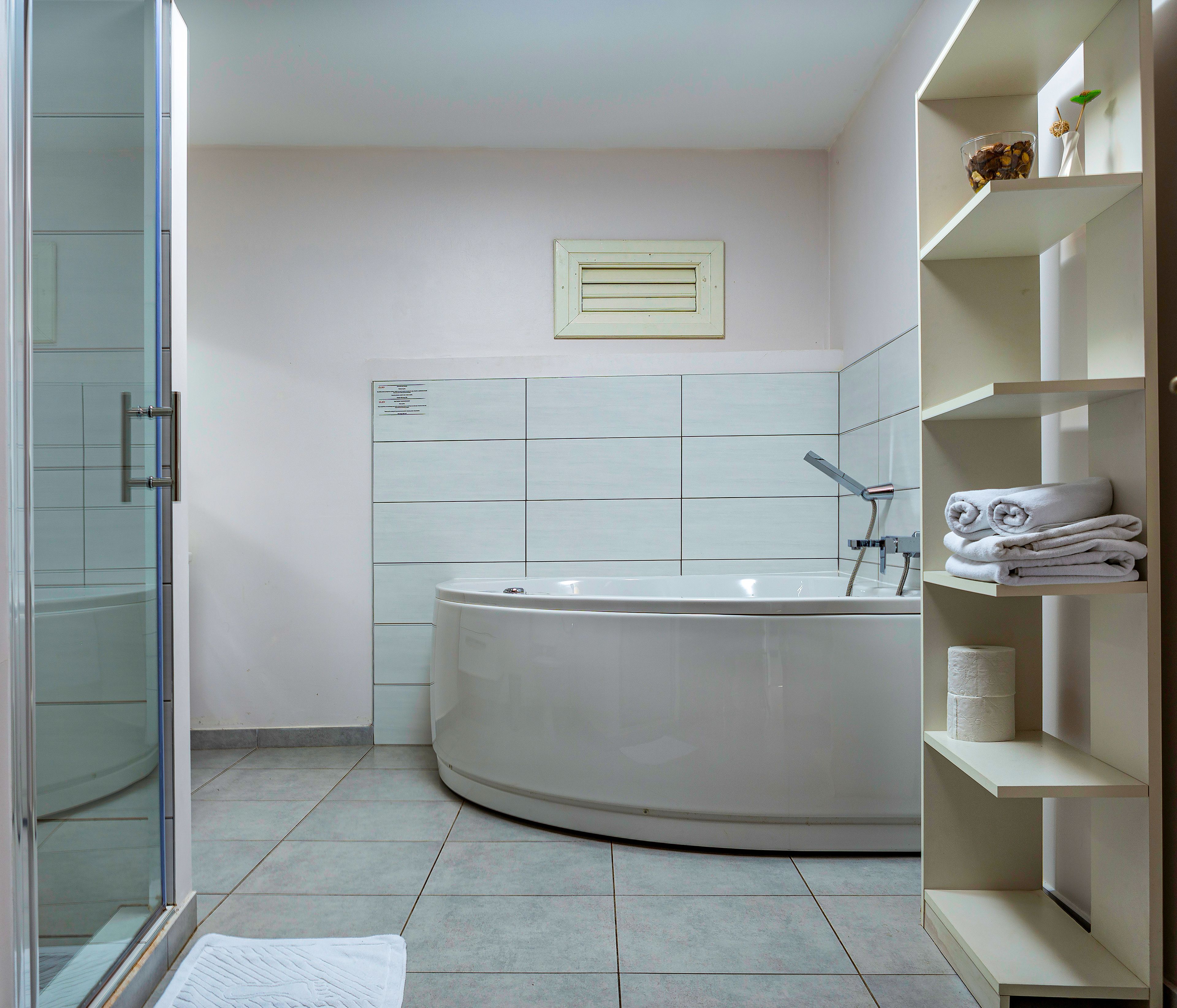 Een moderne badkamer met een vrijstaand bad, een douchecabine met glazen wanden en een inbouwplank met handdoeken.