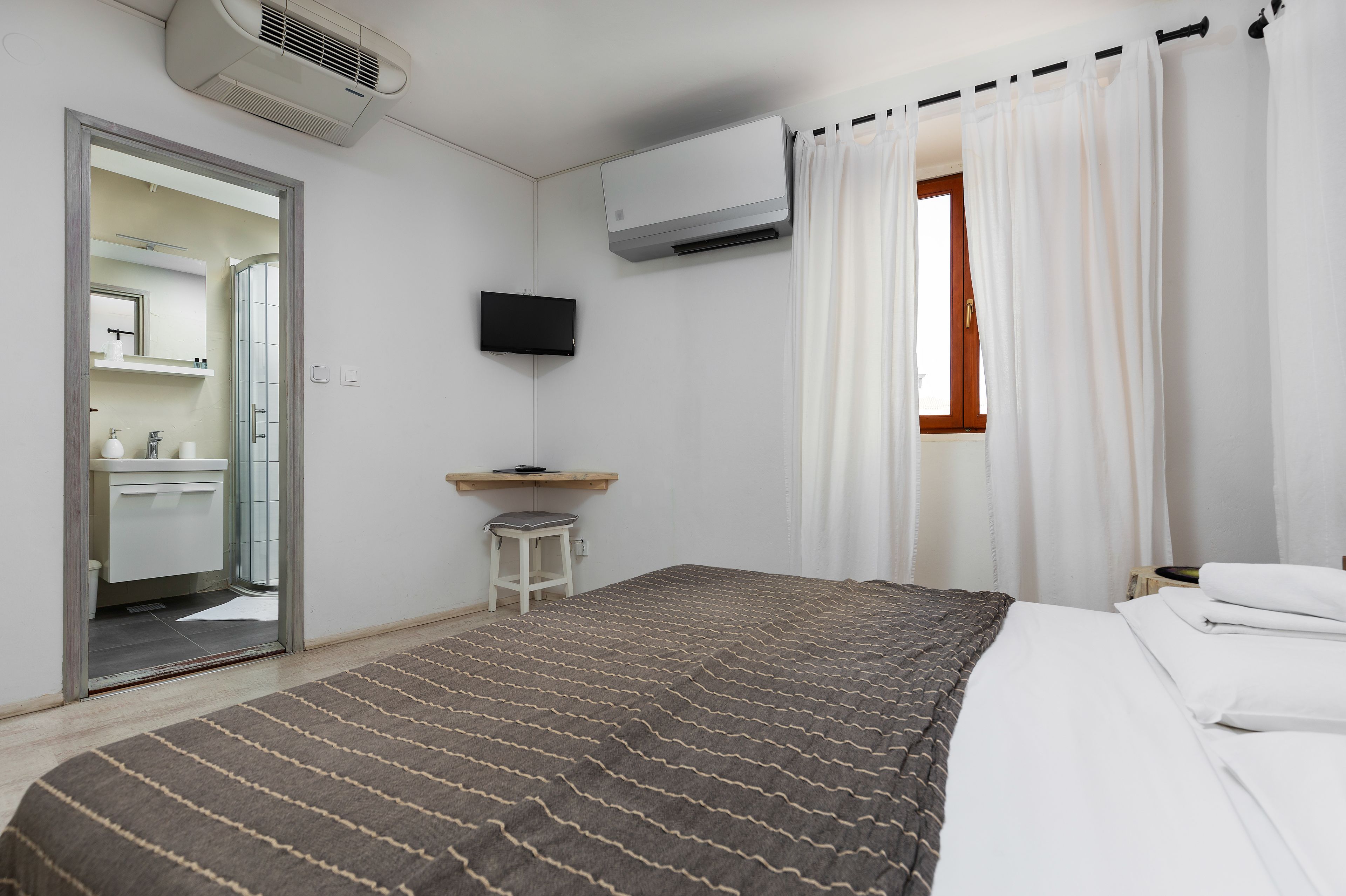 A hotel room with a bed, a desk, a TV, and a window with curtains.