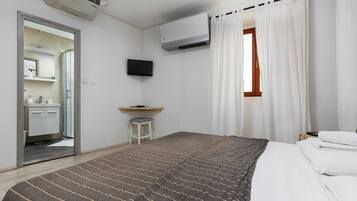 A hotel room with a bed, a desk, a TV, and a window with curtains.