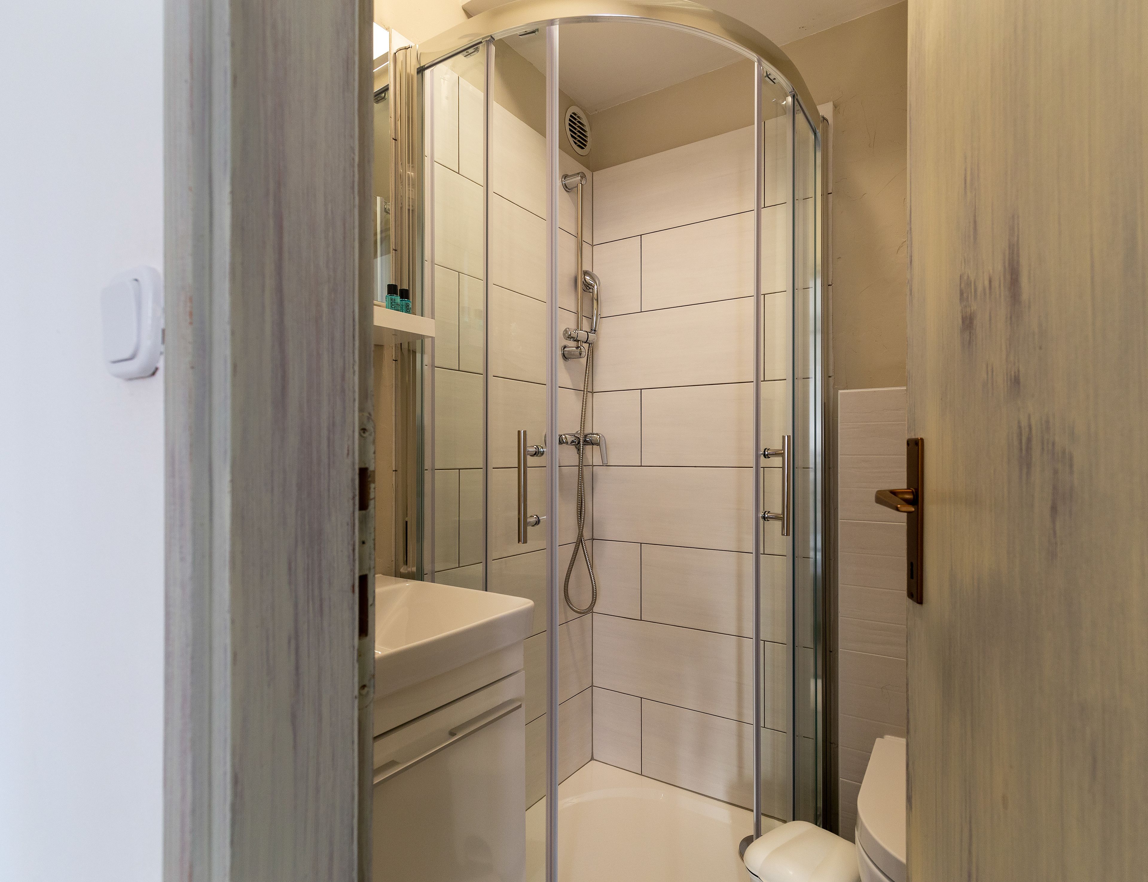 Cabina de ducha con paredes de vidrio, un inodoro blanco y un lavamanos.