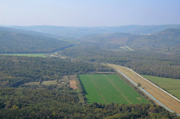 Vista aérea de un paisaje rural con un camino sinuoso, campos verdes y zonas boscosas.